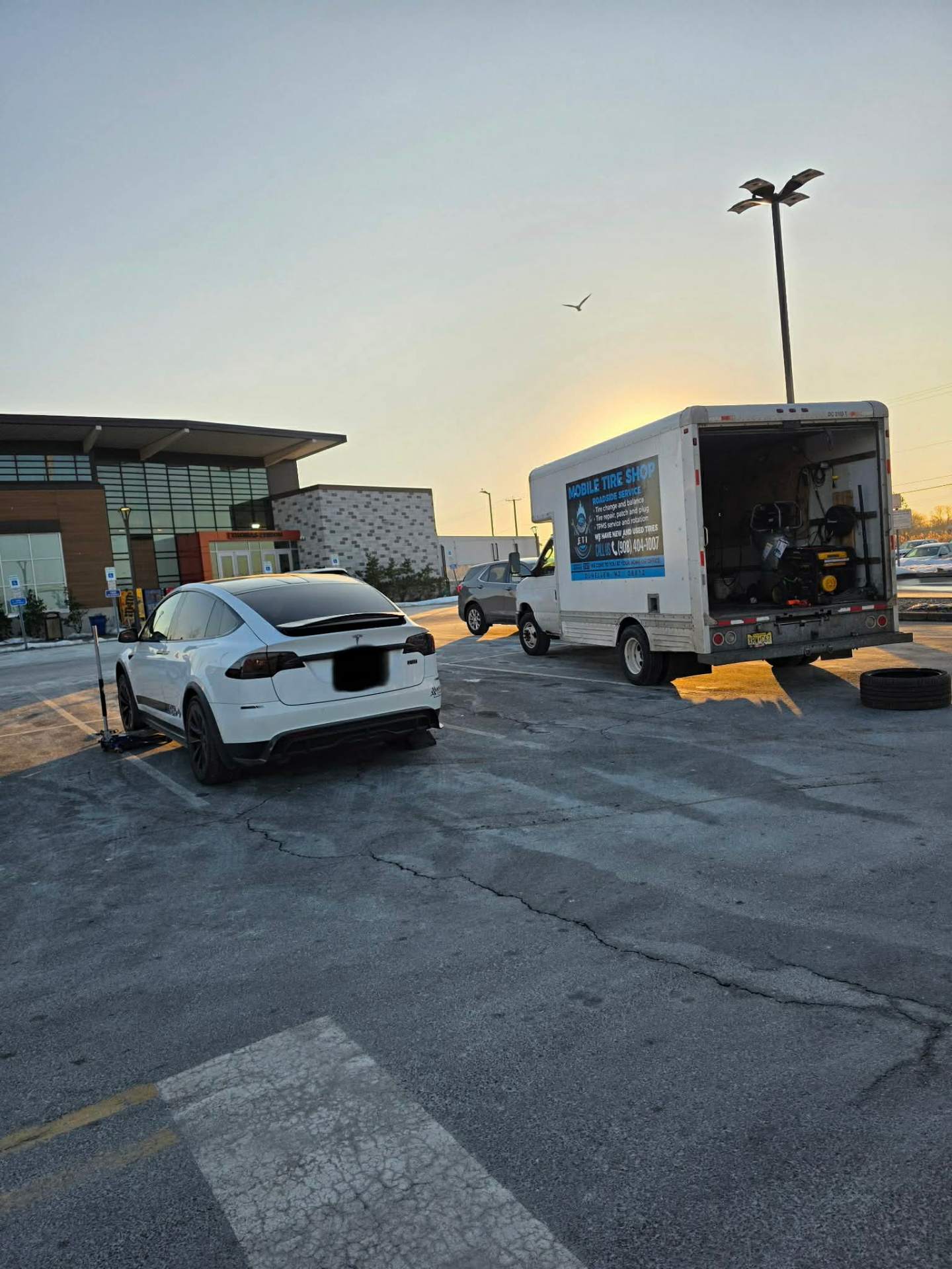 Mobile tire shop truck servicing a Tesla Model X at sunrise